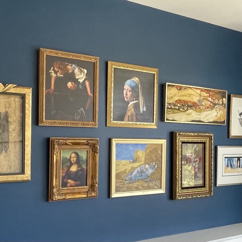 Gilt-framed classical artworks arranged salon-style on a deep blue wall
